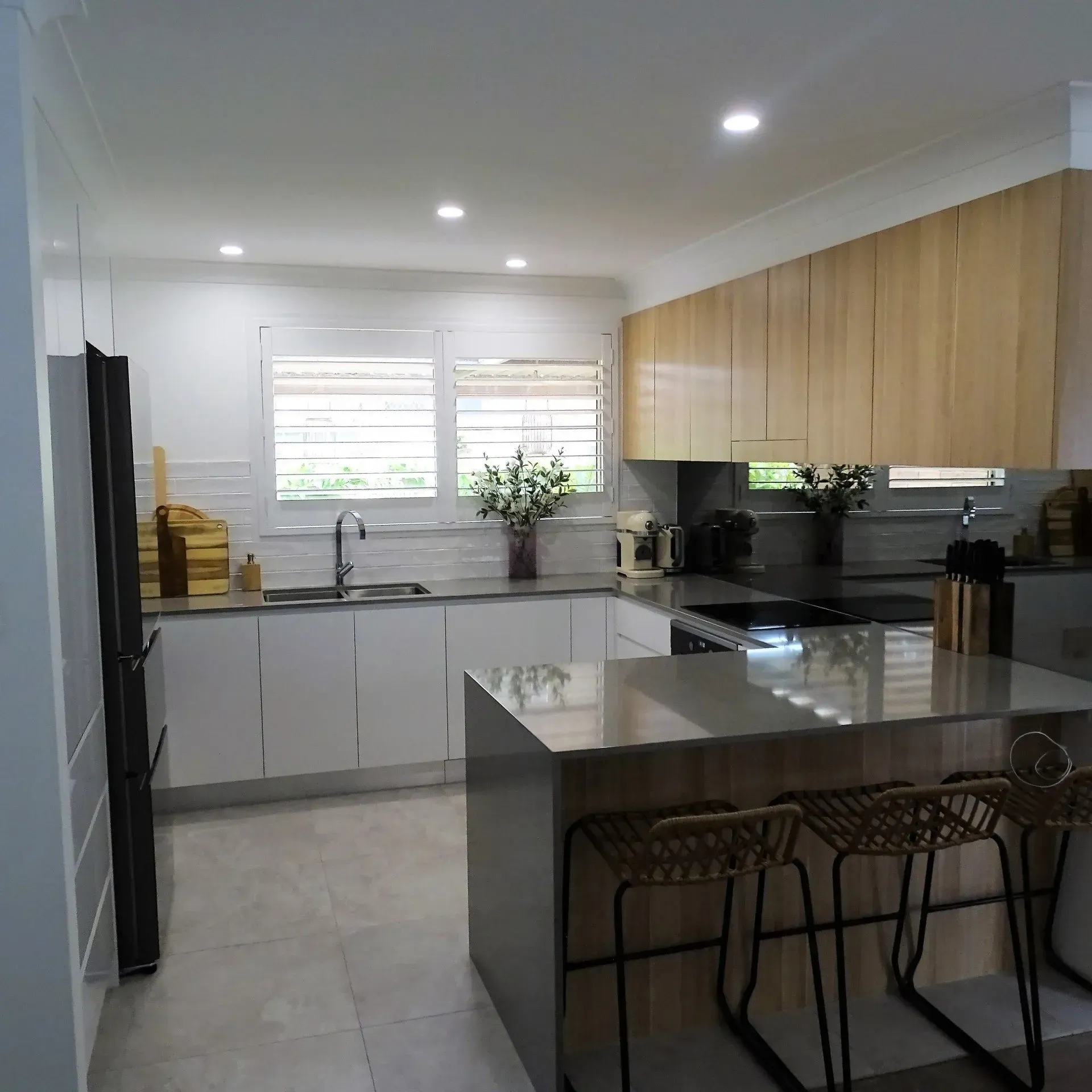 Modern kitchen with white cabinets, wood upper cabinets, island with bar stools, and window with shutters.