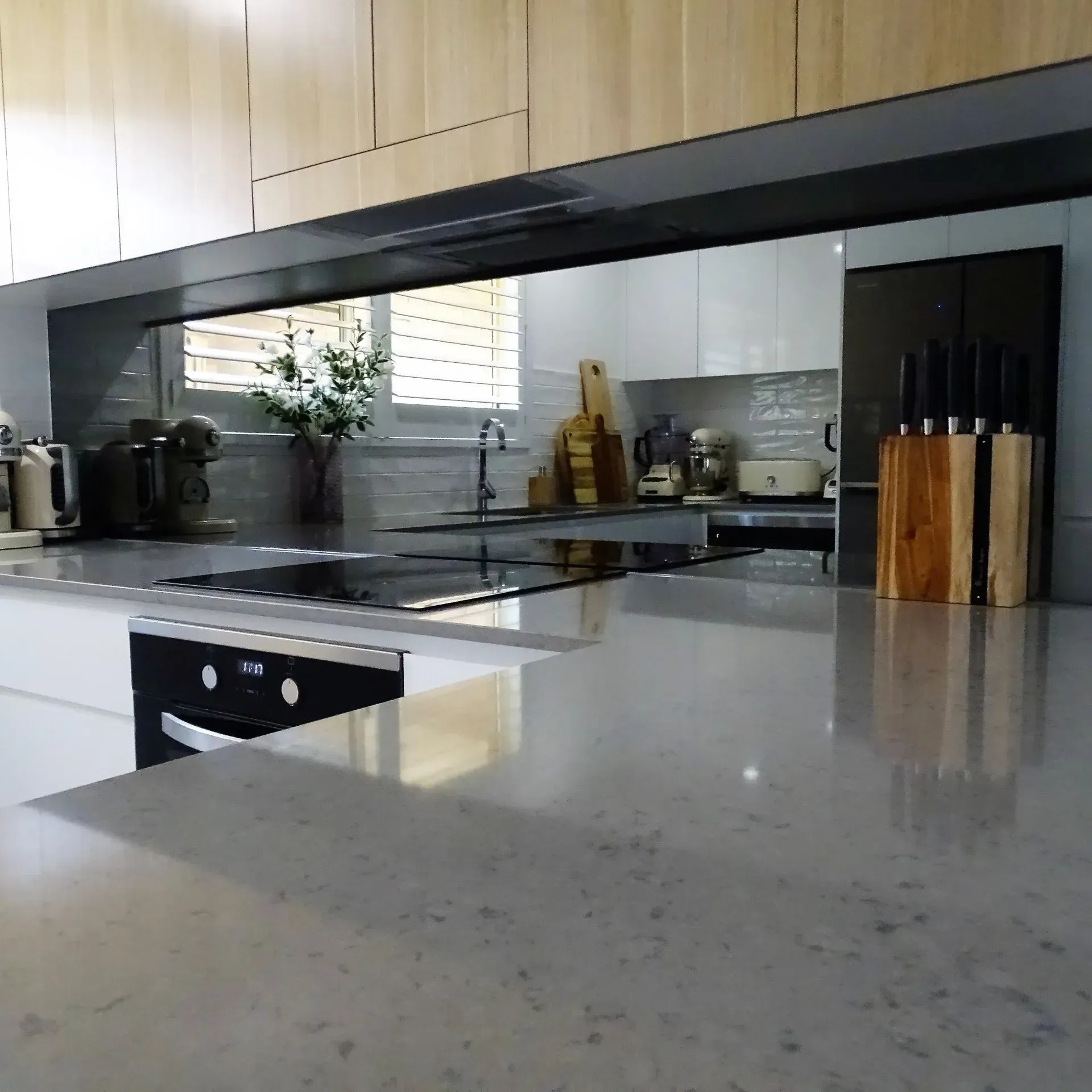 Modern kitchen with light gray countertops, white cabinets, and wooden knife block.