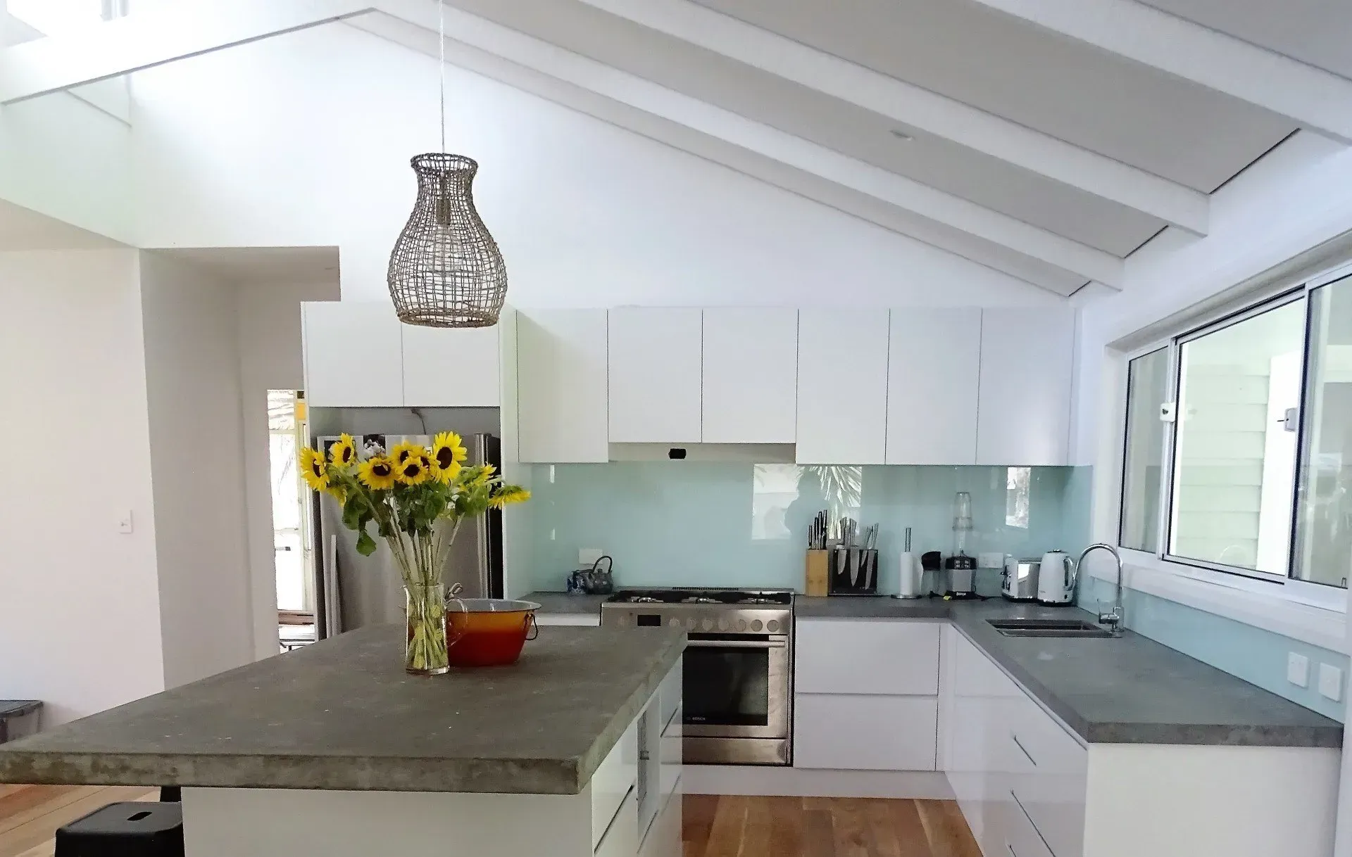 Modern white kitchen with an island, a vase of sunflowers, and a pendant light.