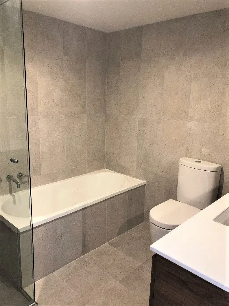 Bathroom with light gray tiled walls, bathtub, toilet, and vanity.