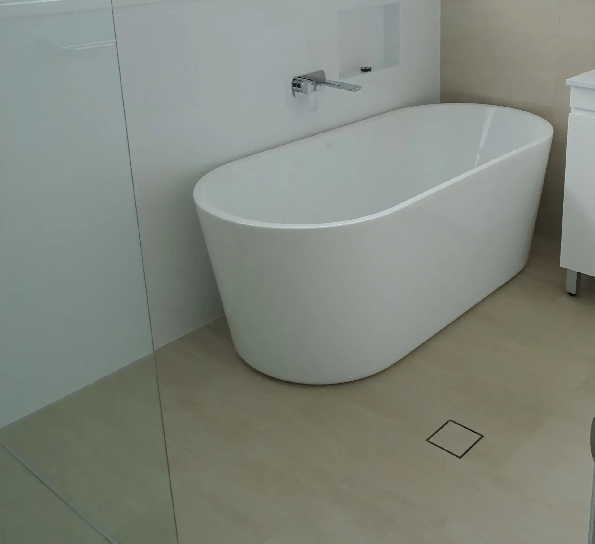 Oval white bathtub in a modern bathroom with beige flooring and chrome faucet.