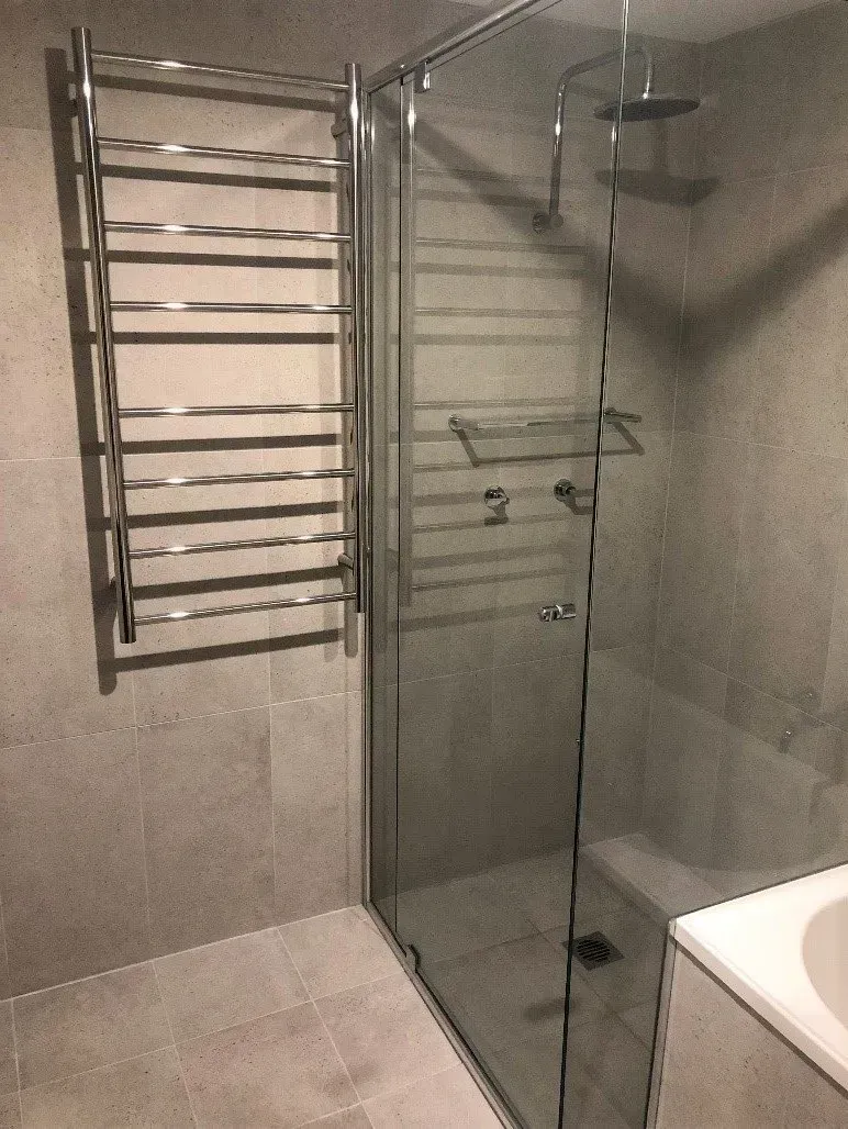 Modern bathroom with a glass shower, heated towel rack, and gray tile.