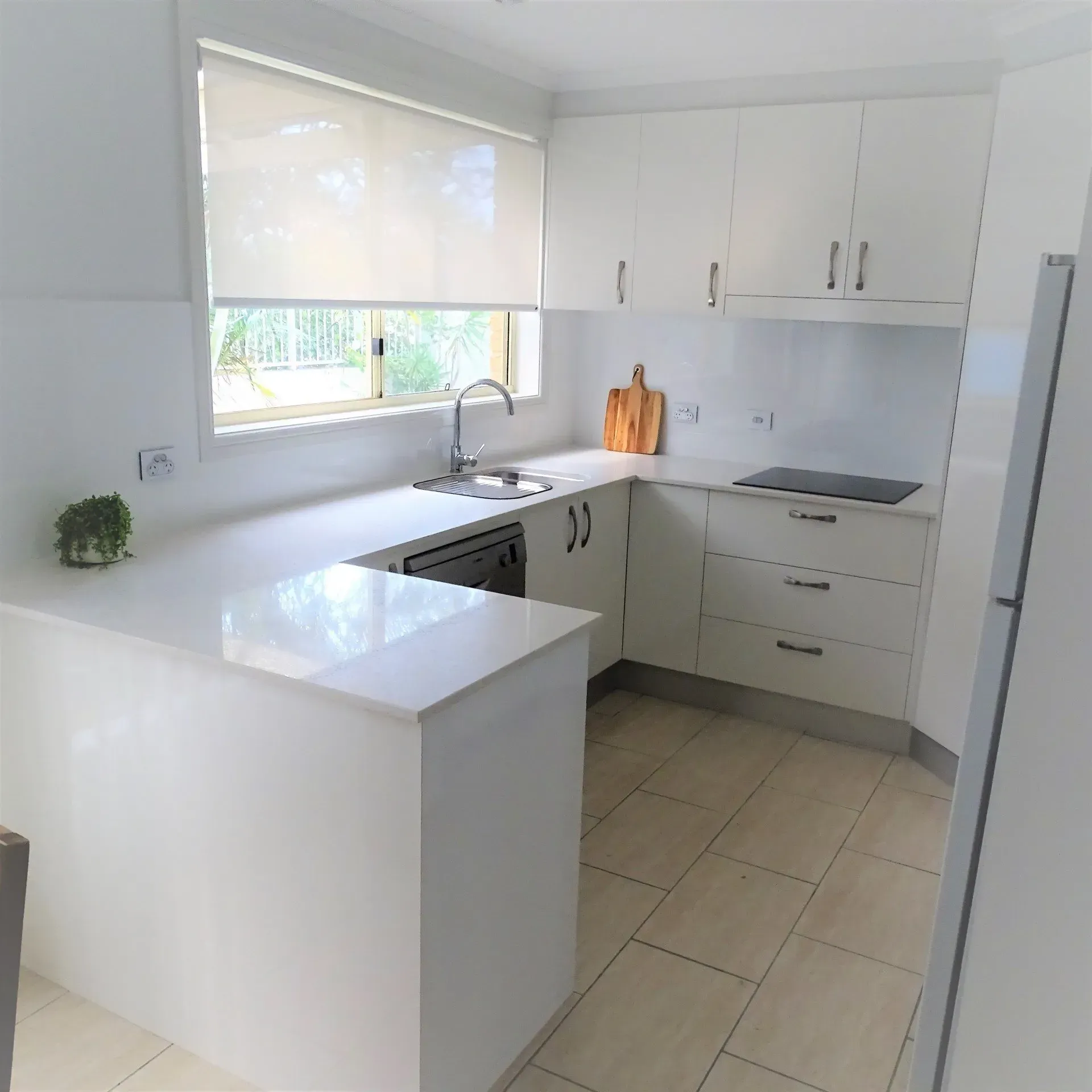 White kitchen with countertops, cabinets, and a window. Includes appliances and a cutting board.