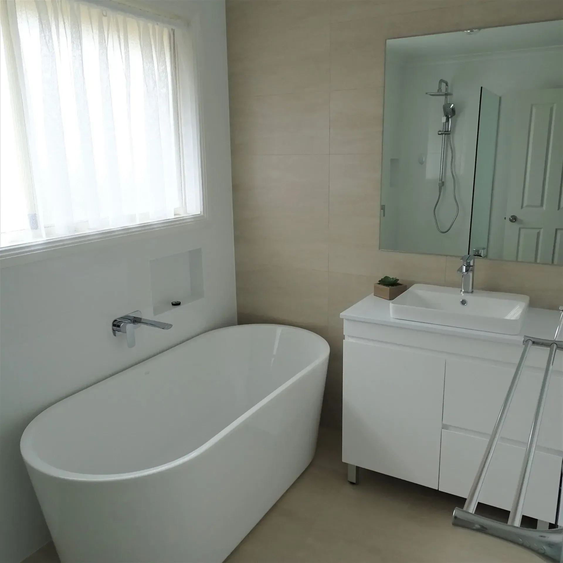 Modern white bathroom with a freestanding tub, vanity, and large mirror.