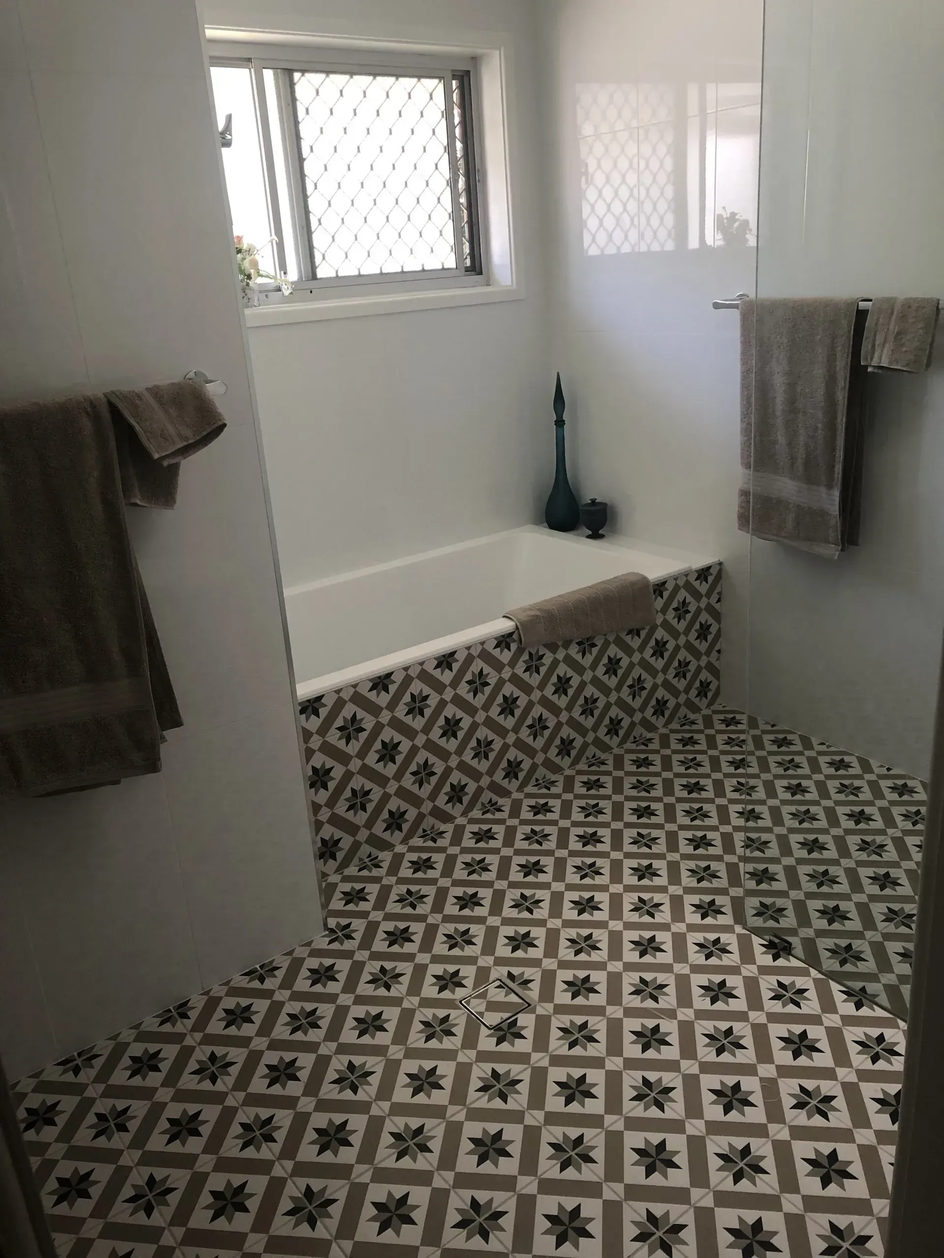 Bathroom with patterned floor tiles and decorative tub surround, white walls, and towels.