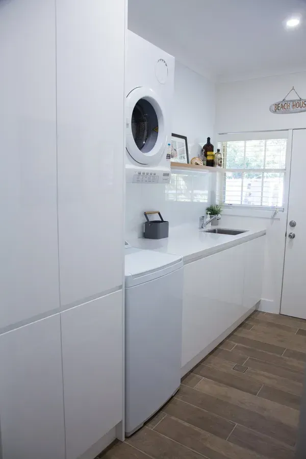 White laundry room with stacked washer/dryer, sink, and cabinetry.