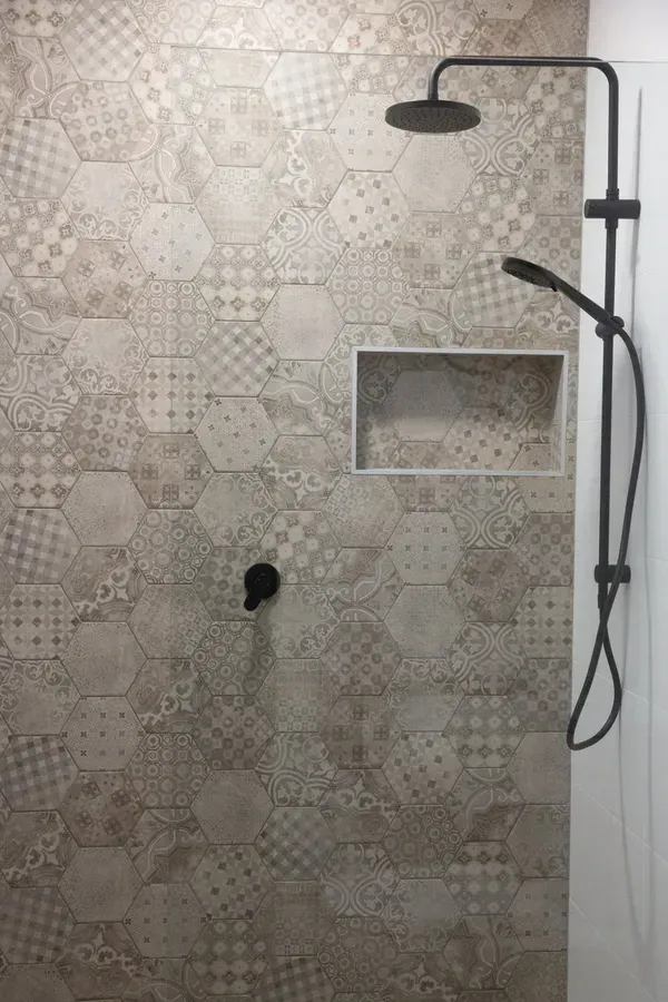 Shower with patterned, beige hexagon tiles, black showerhead and faucet.