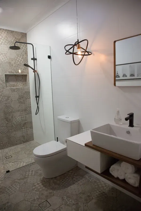 Modern bathroom with shower, toilet, and sink. Black fixtures and a unique light fixture.