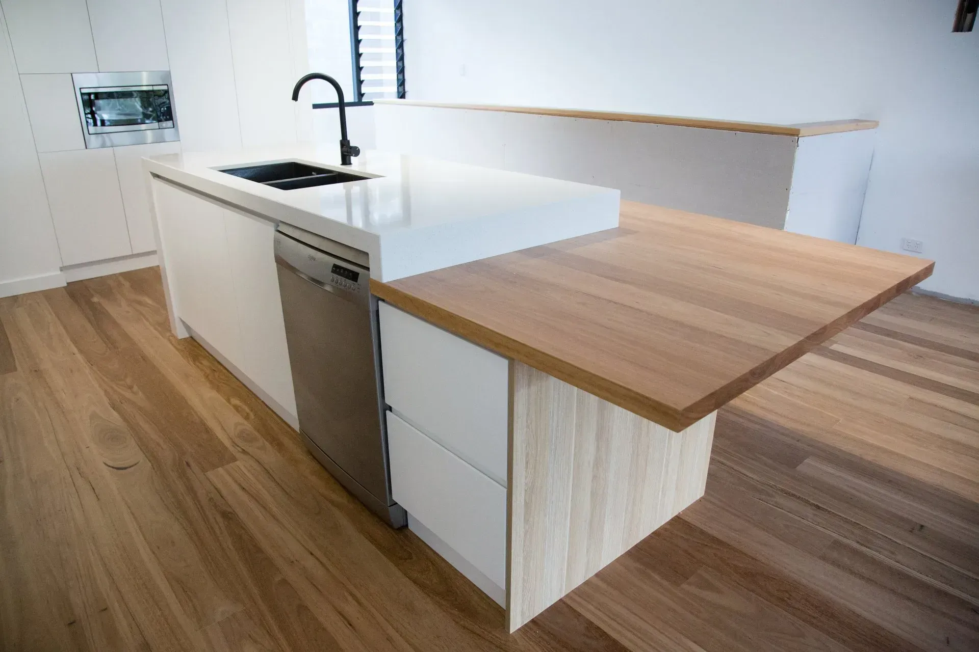 Modern kitchen island with white countertop, dishwasher, and wood-grain countertop extension.