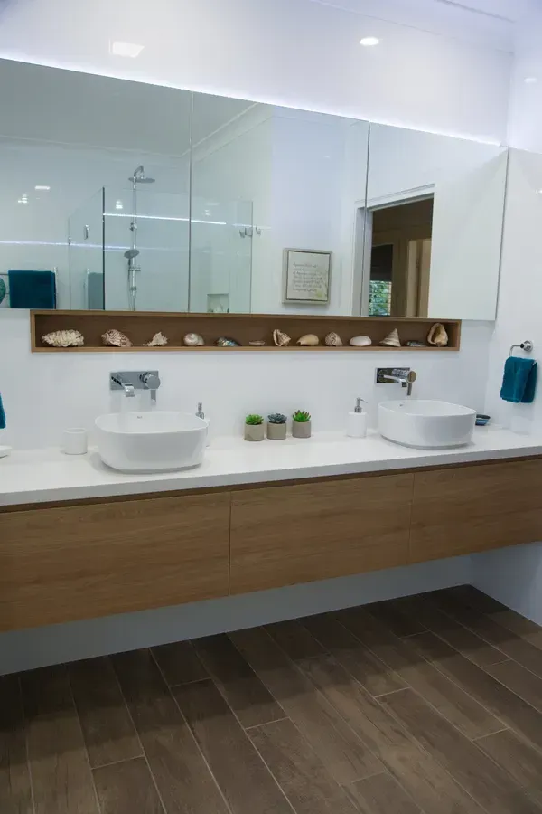 Modern bathroom with wood vanity, white countertops, and floating sinks. Shells line a shelf above the sinks.