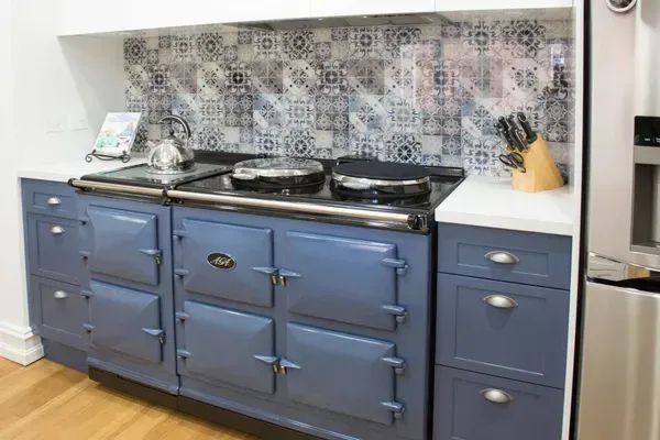 Blue kitchen range with matching cabinets, white countertops, and patterned backsplash.