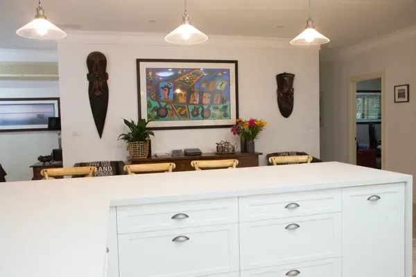 Kitchen with white island, wooden dining table, wall art, and hanging lights.