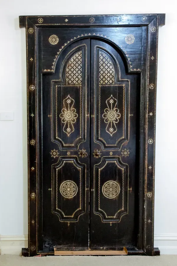 Black wooden double doors with arched top and decorative gold inlay.