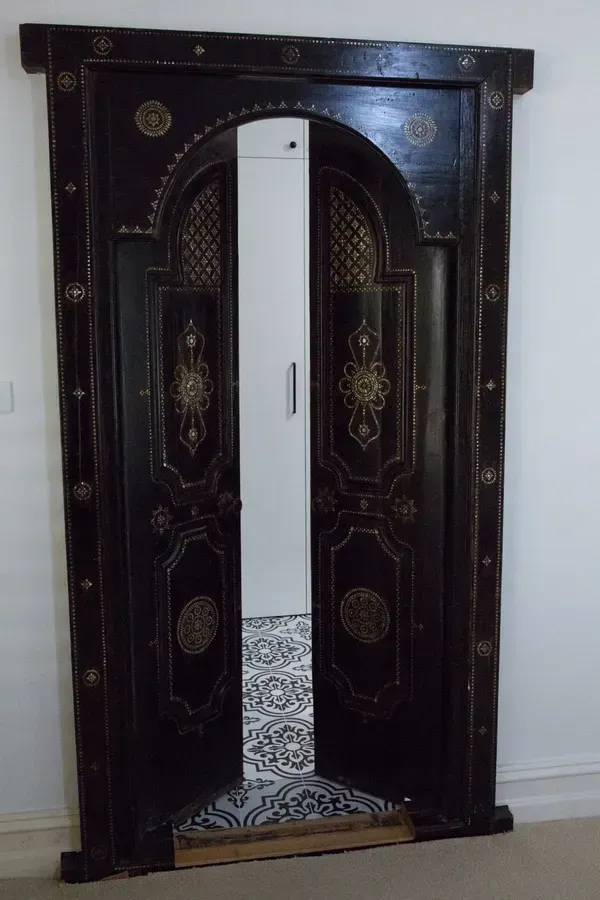 Ornate black wooden door frame with golden embellishments, open, revealing a white room.