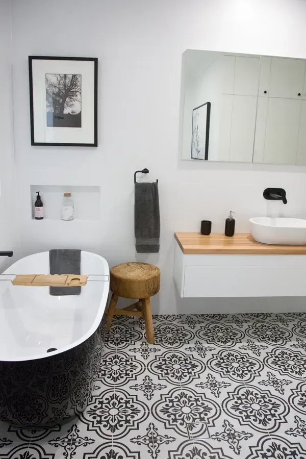 Bathroom with black and white patterned floor, a white bathtub, and a wood vanity.
