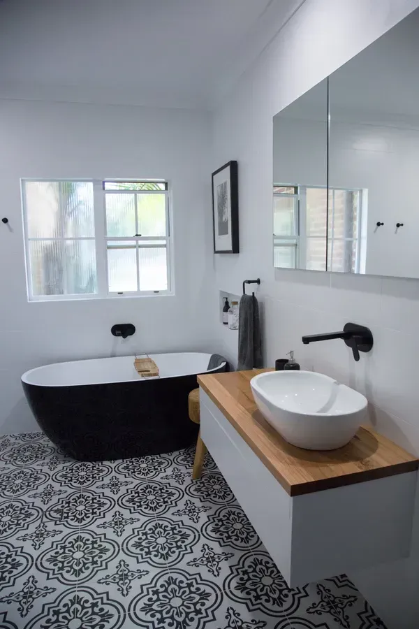 Black and white bathroom with patterned floor, black tub, wooden vanity, and large mirror.