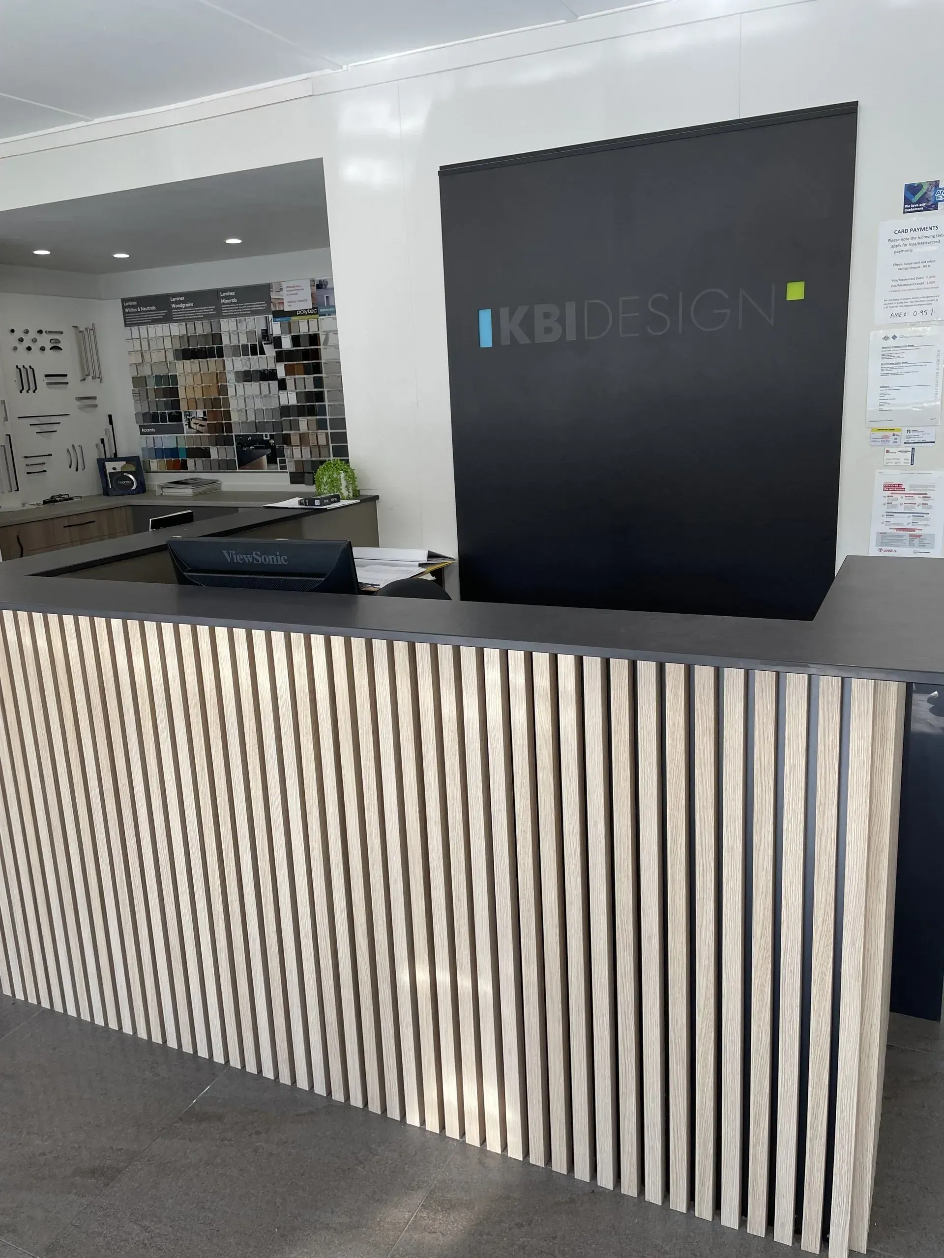 Reception desk with wooden slat front, black countertop, black wall with company logo, interior.
