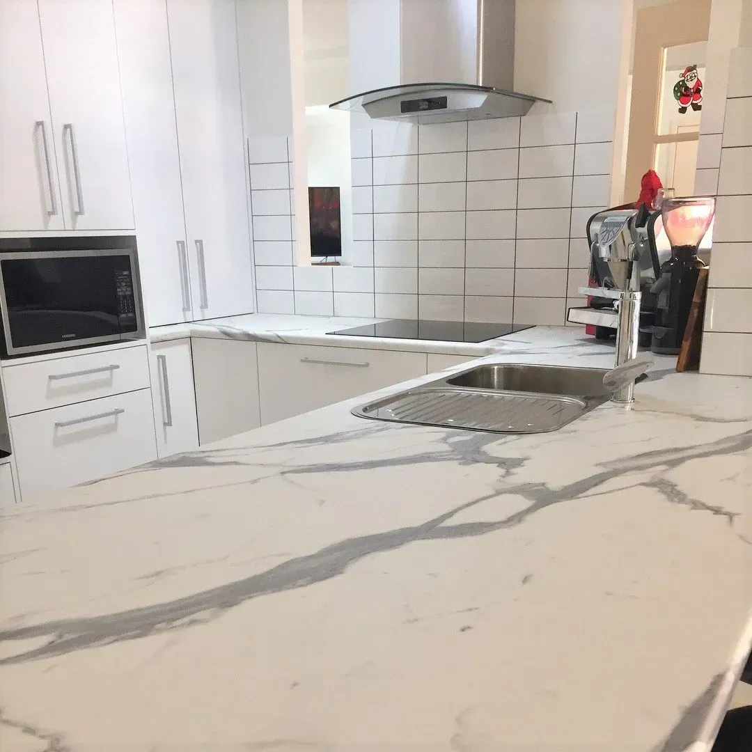 White kitchen with marble countertops, stainless steel sink, microwave, and range hood.