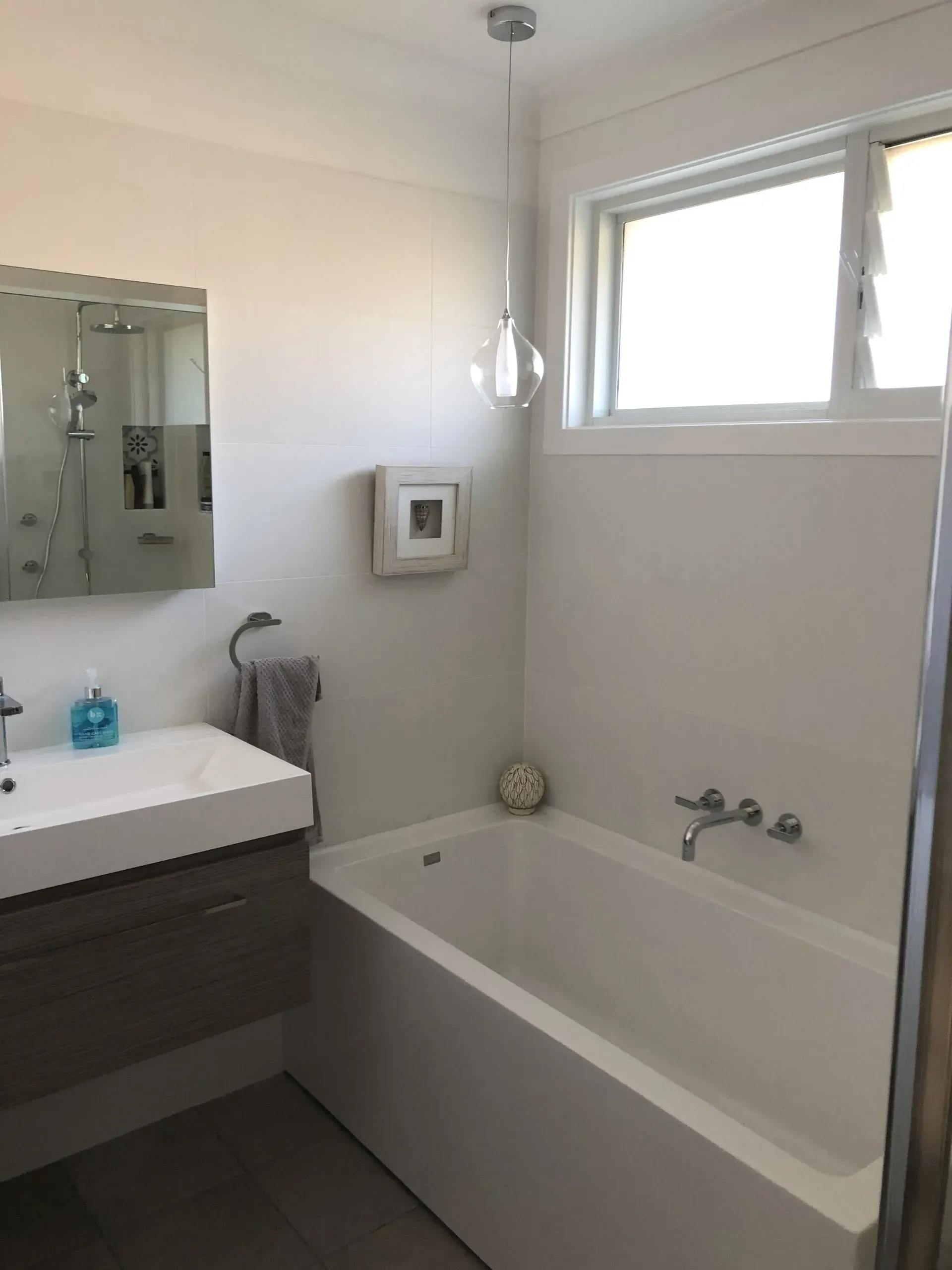 Bathroom with a white bathtub, sink, and window, neutral colors.