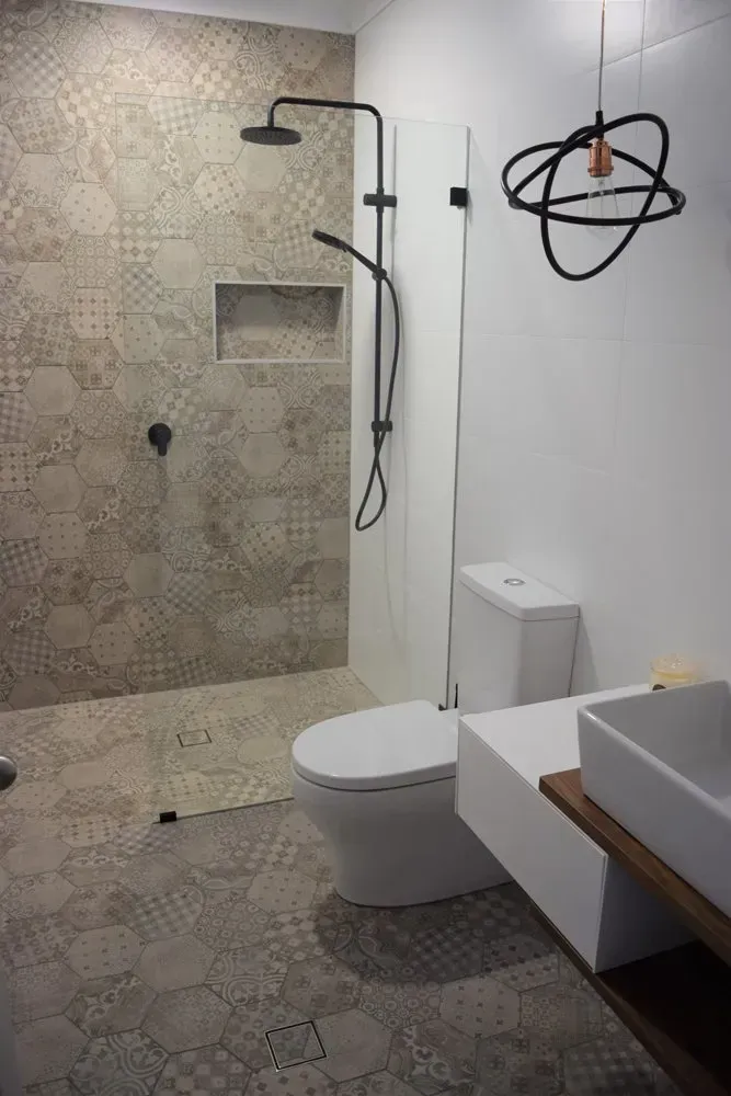 Modern bathroom with patterned tile shower, black fixtures, white toilet, and a decorative light fixture.