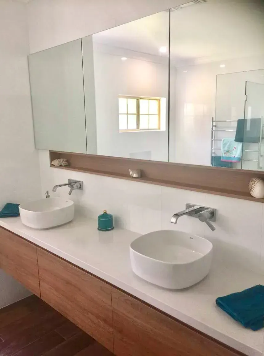 Modern bathroom with double sinks, white countertop, wooden vanity, and large mirror.