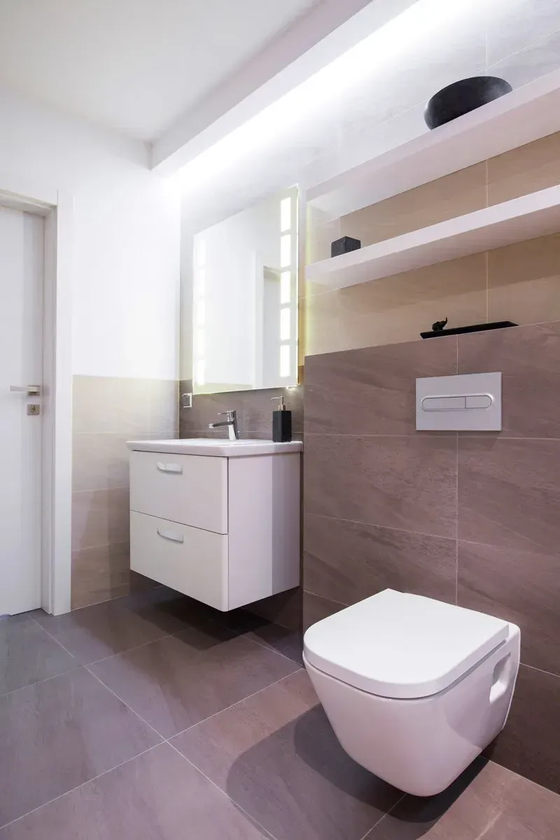 Modern bathroom with a floating white toilet and vanity. Grey tiled floor and wall.