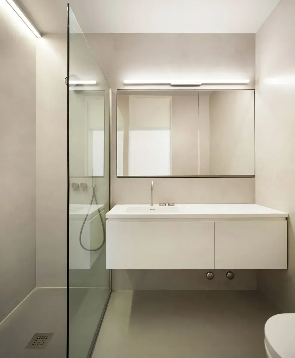 Modern bathroom with a white floating vanity, large mirror, glass shower, and neutral walls.