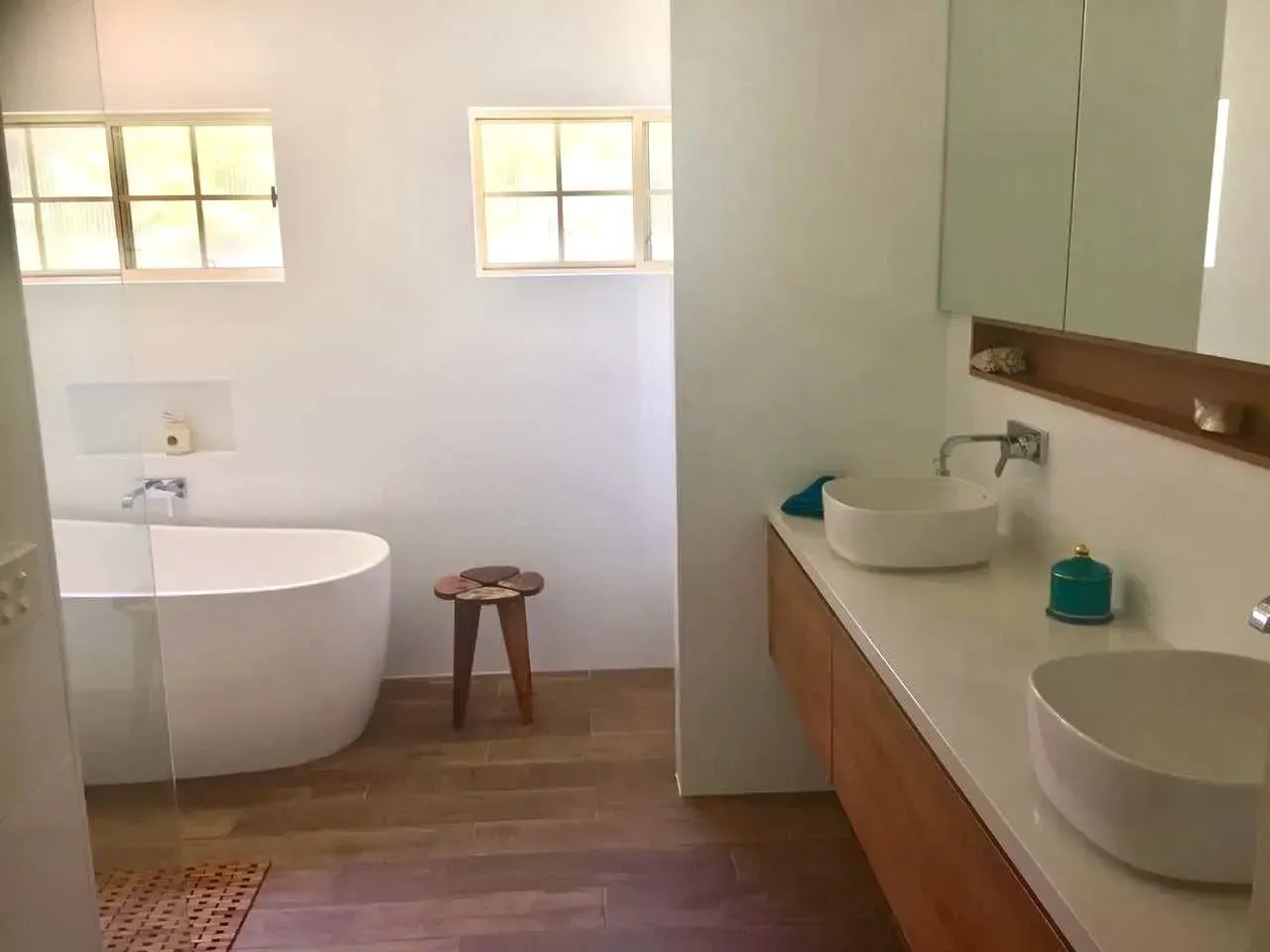 Bathroom with white tub, two vessel sinks, wooden vanity, and windows.