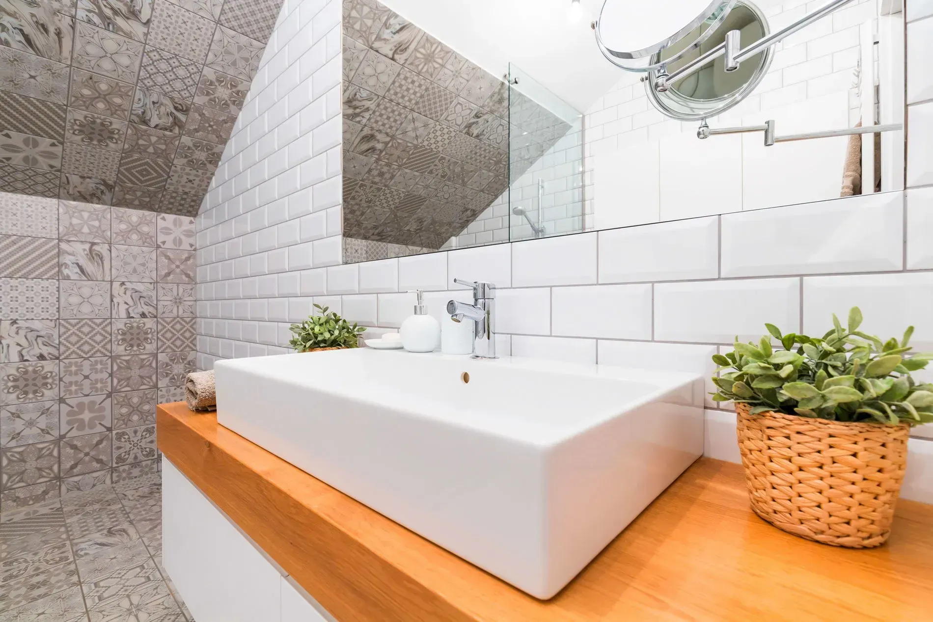 White bathroom with rectangular sink on wooden counter, plants, and tiled walls.