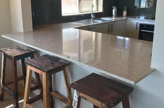Three wooden stools at a kitchen counter. Beige countertop, sink and oven visible.