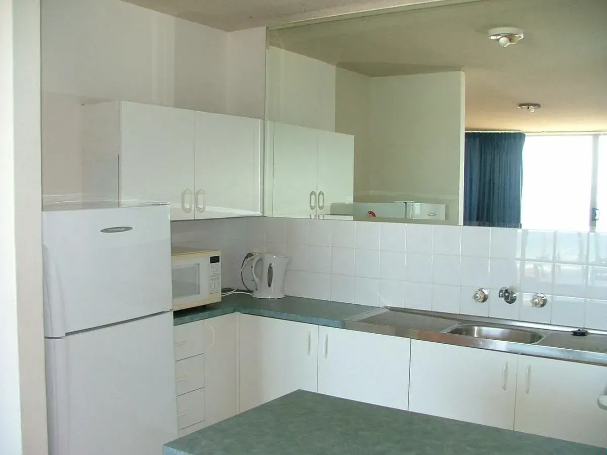 White kitchen with cabinets, appliances, and countertop; mirror reflects window with blue curtain.
