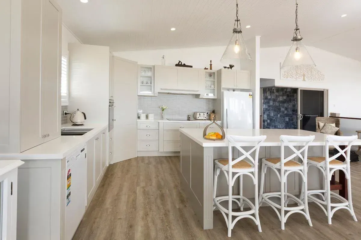 Bright, airy kitchen with white cabinets, island, and bar stools. Wooden floors.