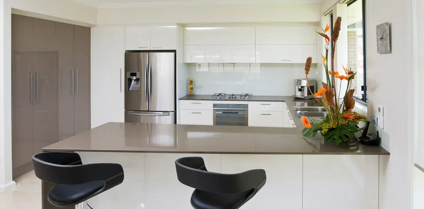 Modern kitchen with a stainless steel refrigerator, a gray countertop, and black bar stools.