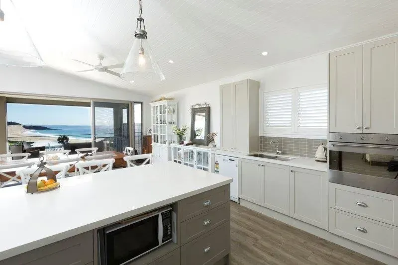 Bright kitchen with ocean view: white cabinets, gray island, microwave, oven, and open to deck with seating.