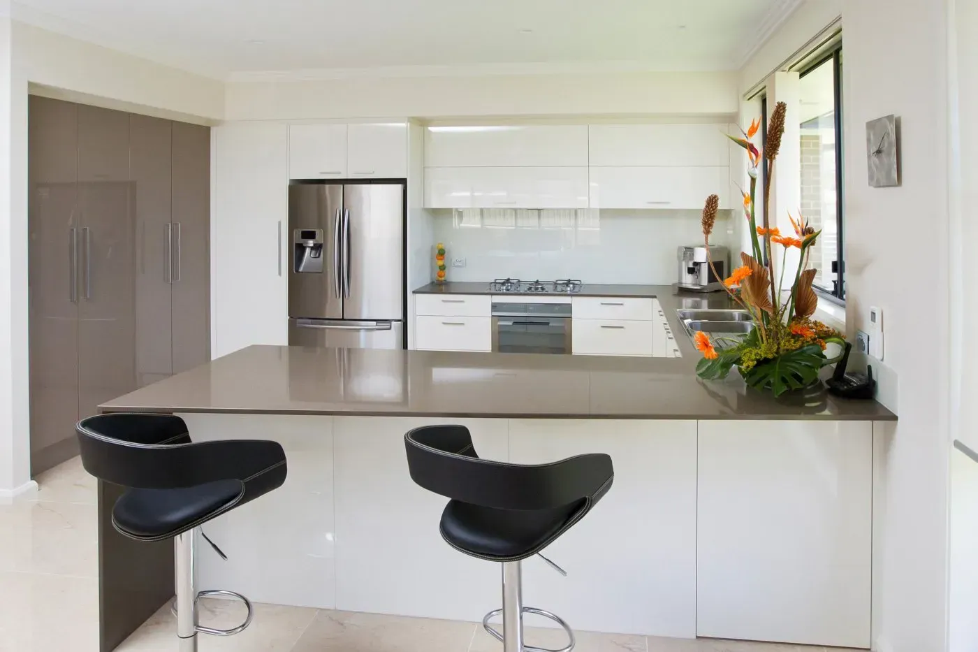 Modern kitchen with island, stainless steel appliances, white cabinets, and two black bar stools.