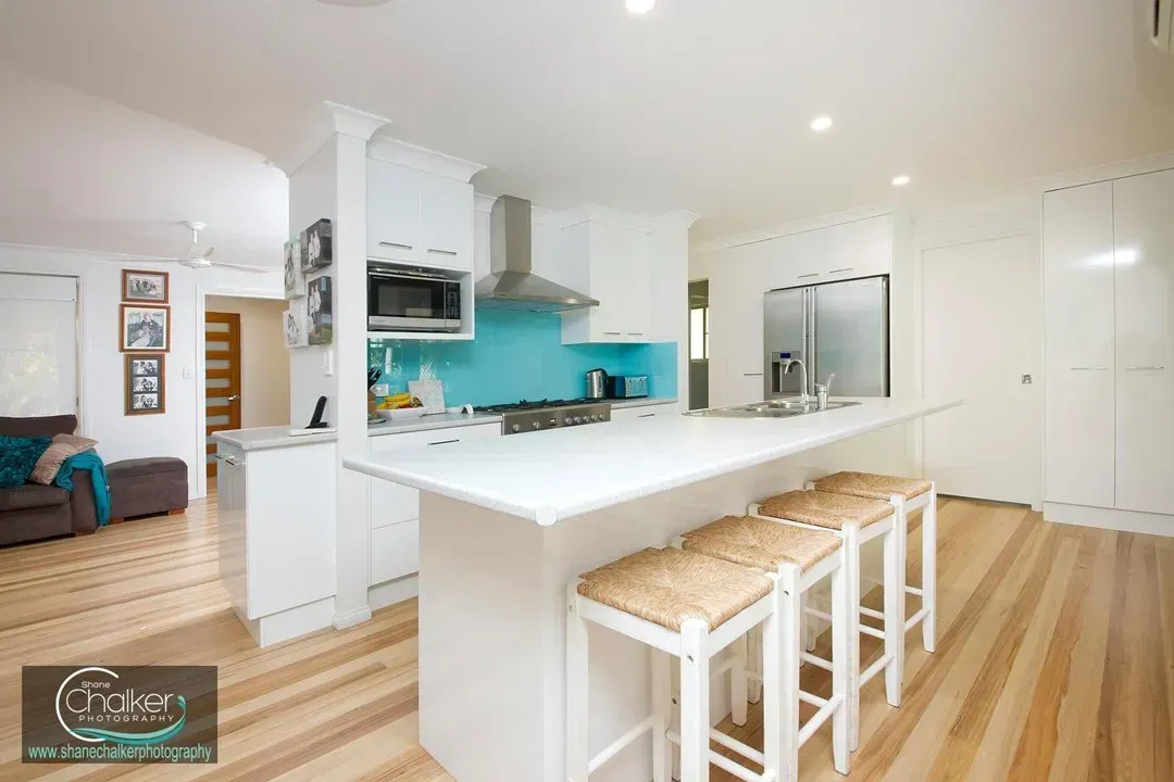 Bright kitchen with white cabinets, blue backsplash, island with stools, and wood flooring.