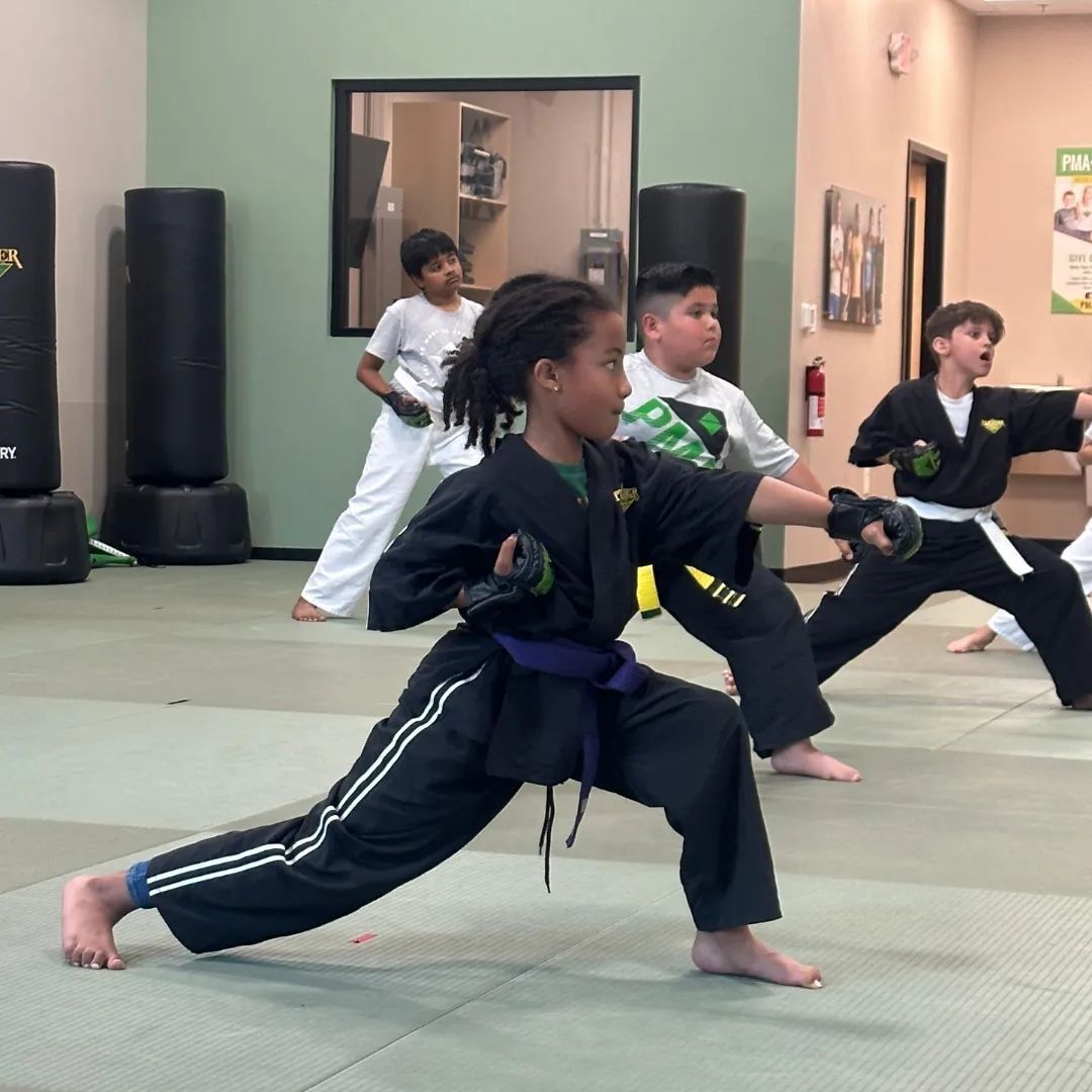 A group of children are practicing karate with a teacher in a gym.
