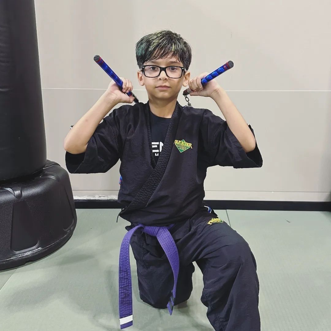 A man is kneeling down next to a young boy in a taekwondo class.
