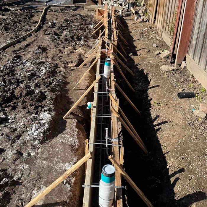 A foundation of a house under construction with red pipes in the sand.