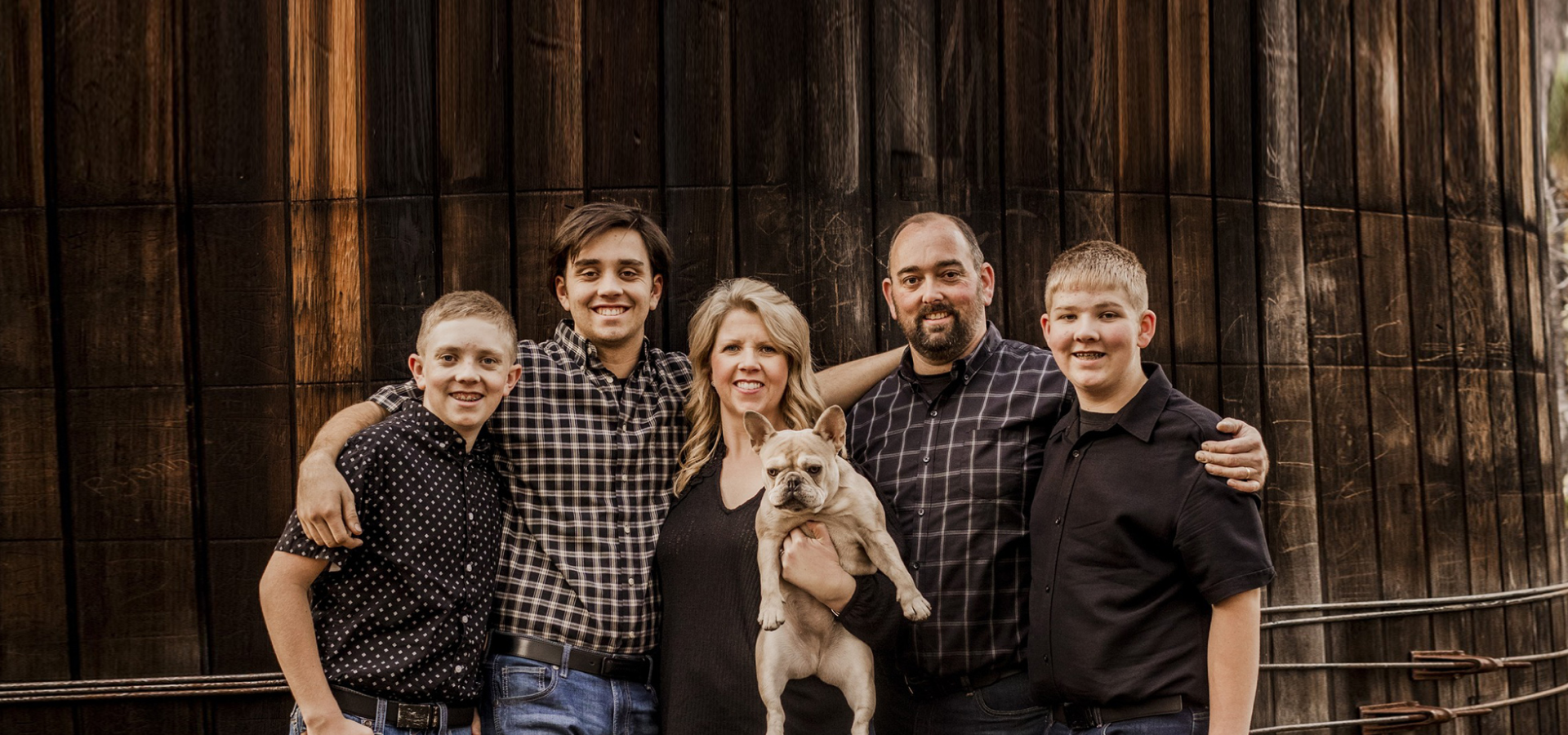 A family is posing for a picture with a dog in front of a wooden wall. | J&H Automotive Inc