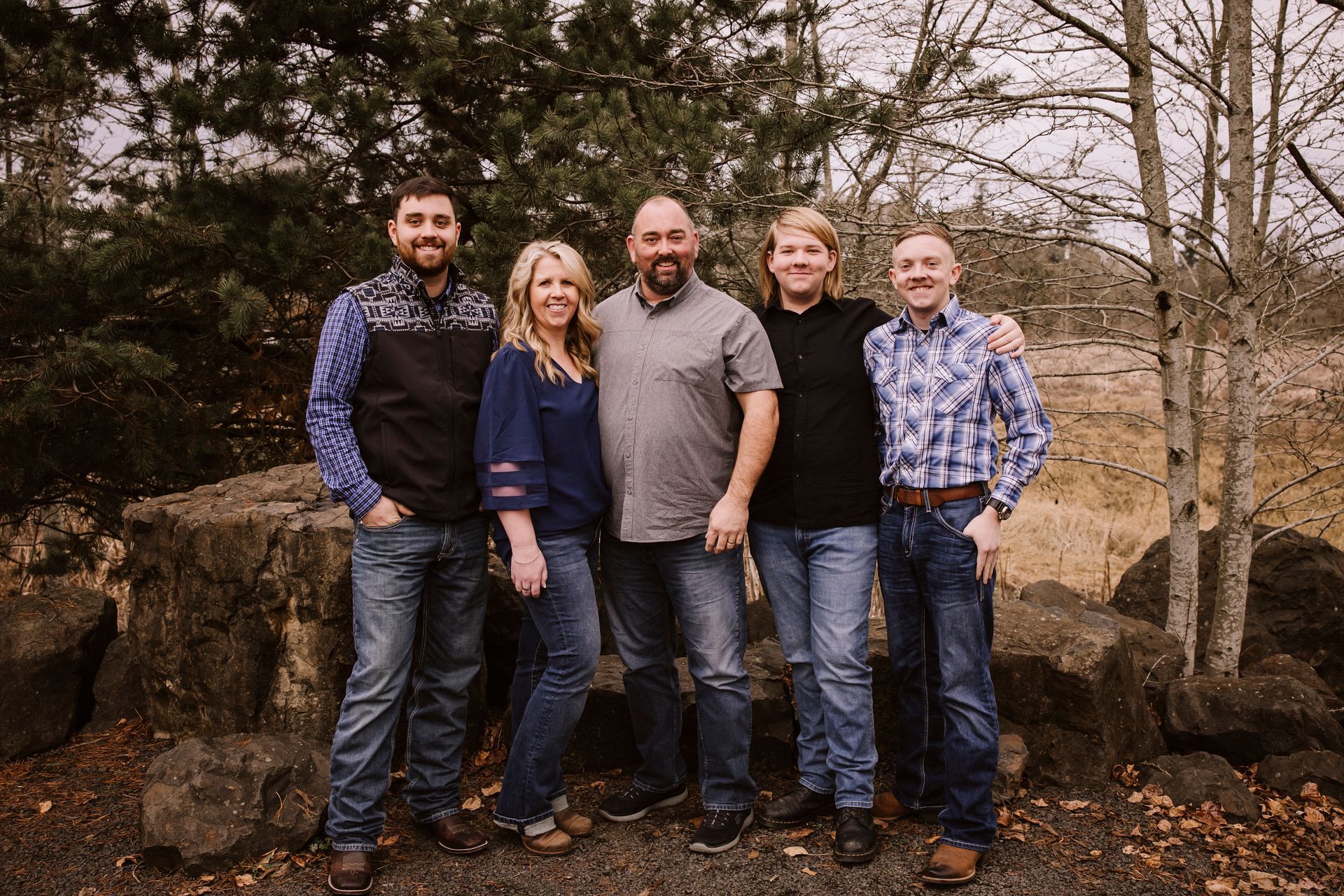 A family is posing for a picture with a dog in front of a wooden wall. | J&H Automotive Inc