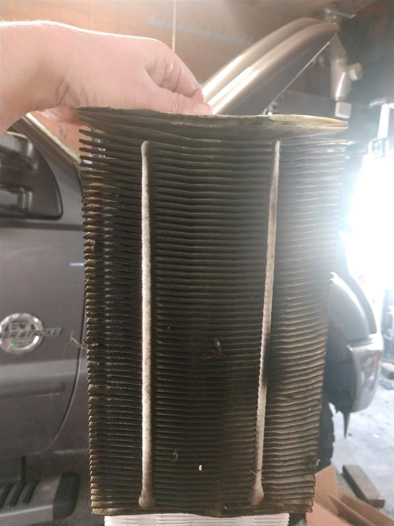 A person is holding an air filter in front of a car. | 