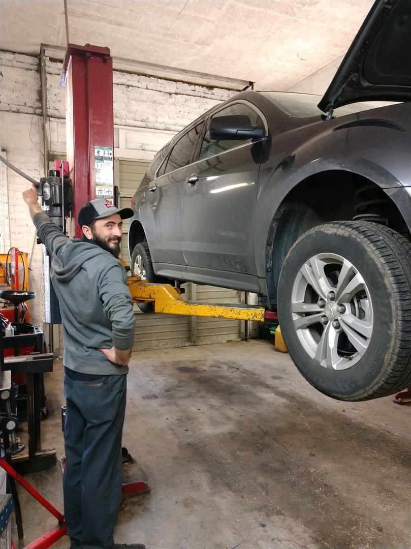 A man is standing next to a car on a lift in a garage. | J&H Automotive