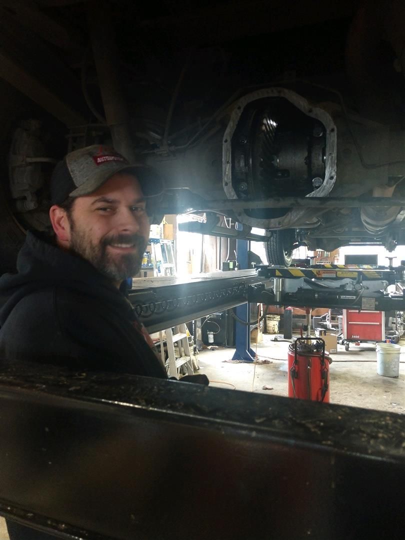 A man is standing under a car in a garage. | J&H Automotive