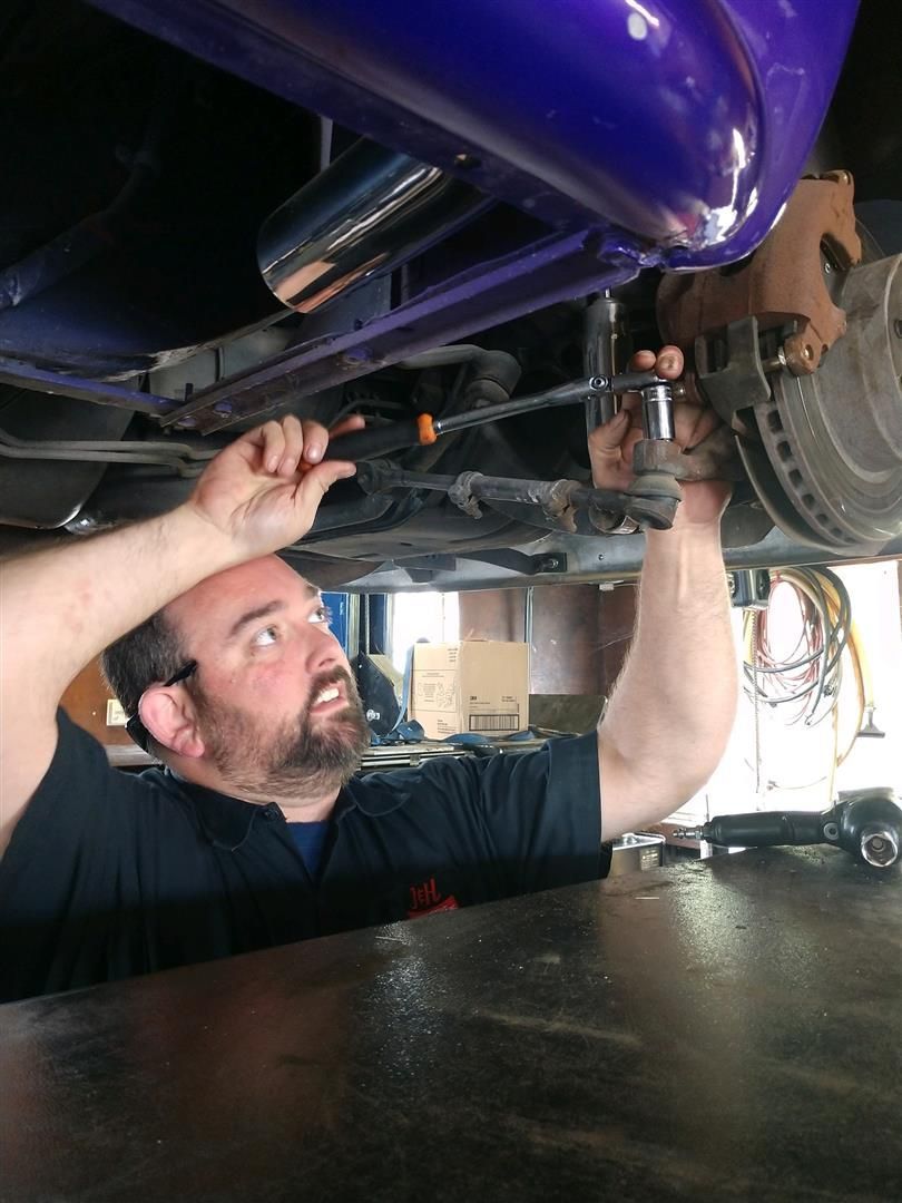 A man is working under a purple car with a screwdriver. | J&H Automotive