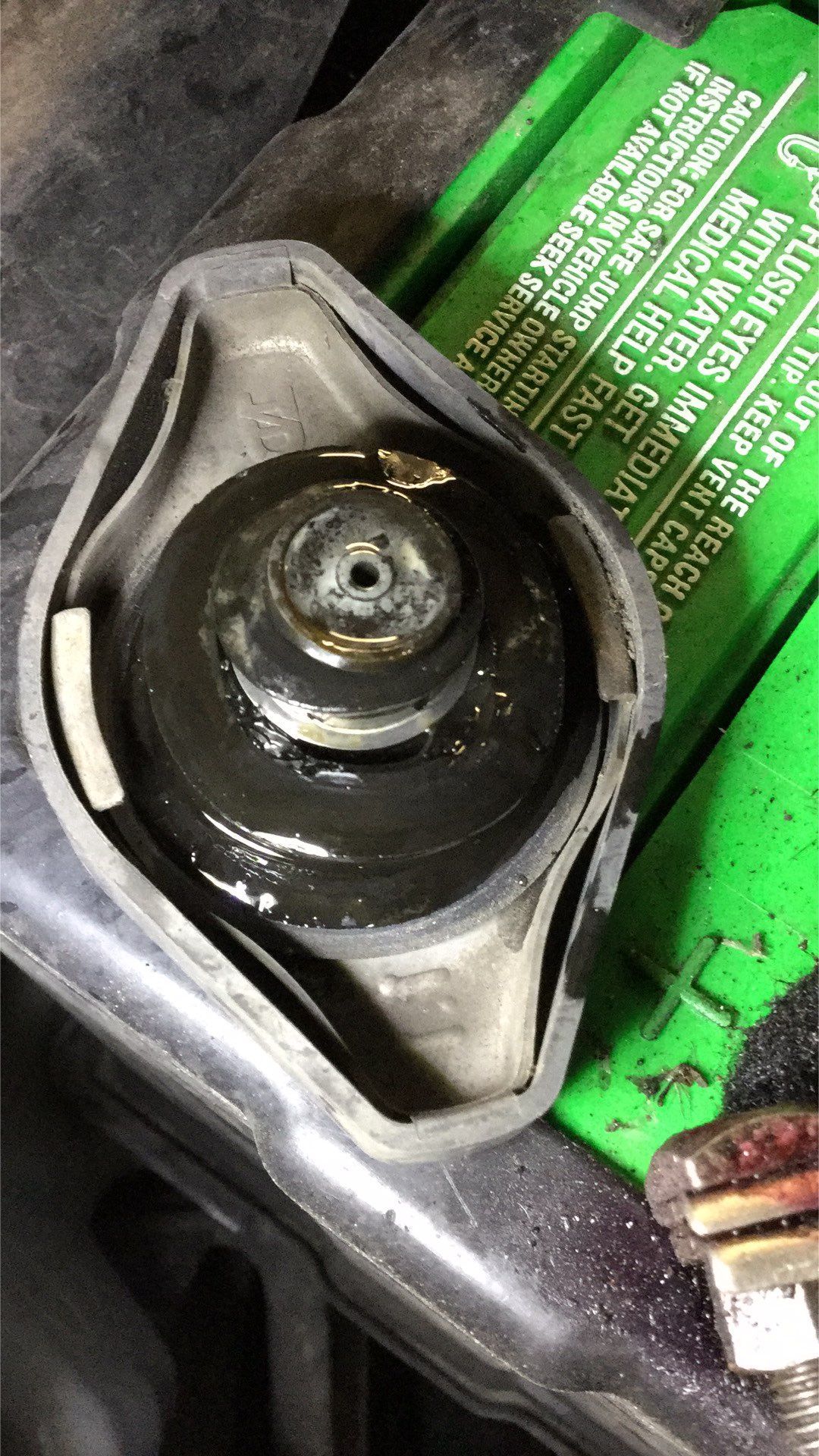 A radiator cap is sitting on top of a green battery. | J&H Automotive