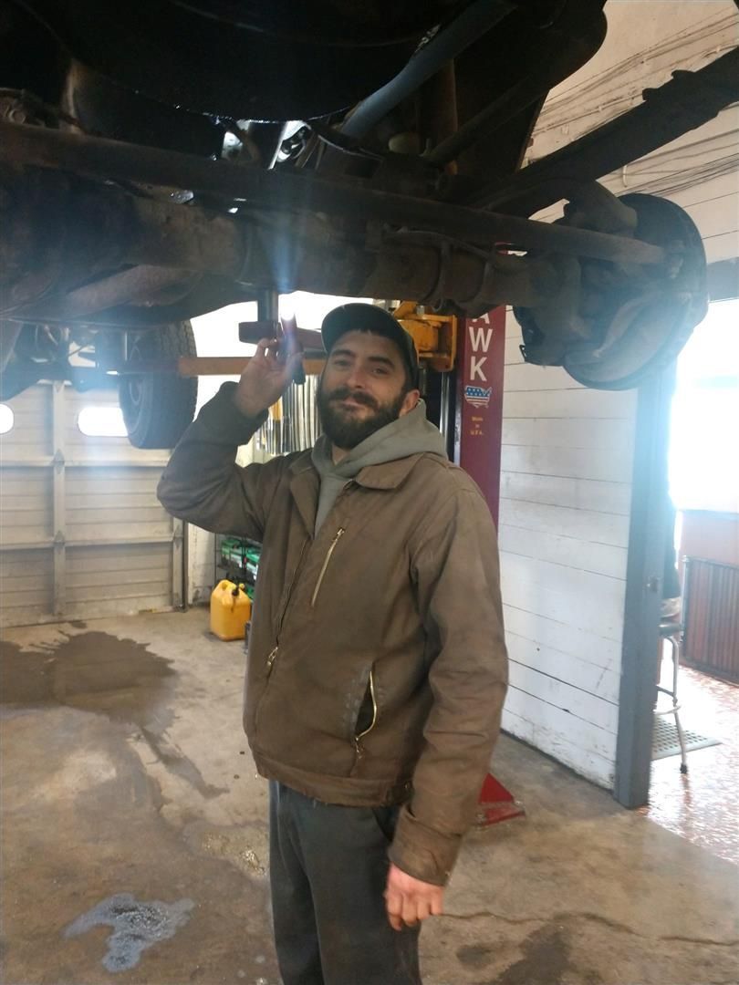 A man with a beard is standing under a car in a garage. | J&H Automotive