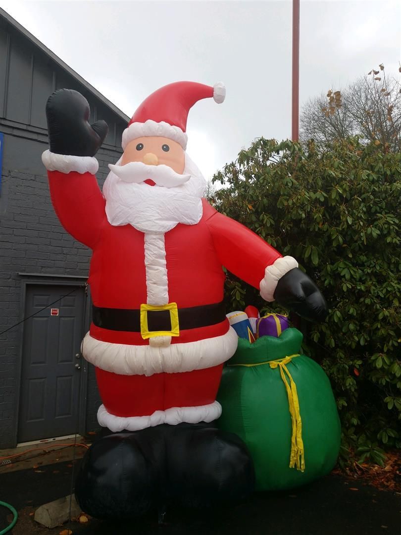 A large inflatable santa claus holding a green bag of presents | J&H Automotive