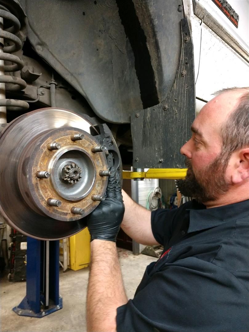 A man wearing black gloves is working on a brake disc on a car. | J&H Automotive