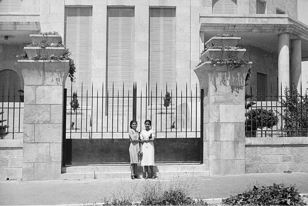 Stone house with arched entrance and exterior staircase, surrounded by greenery.